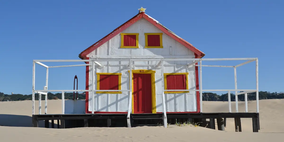 Colourful beach huts on the Costa da Caparica shore Colourful wooden beach houses on the Costa da Caparica sand, with orange terracotta roofs and blue, green and grey facades